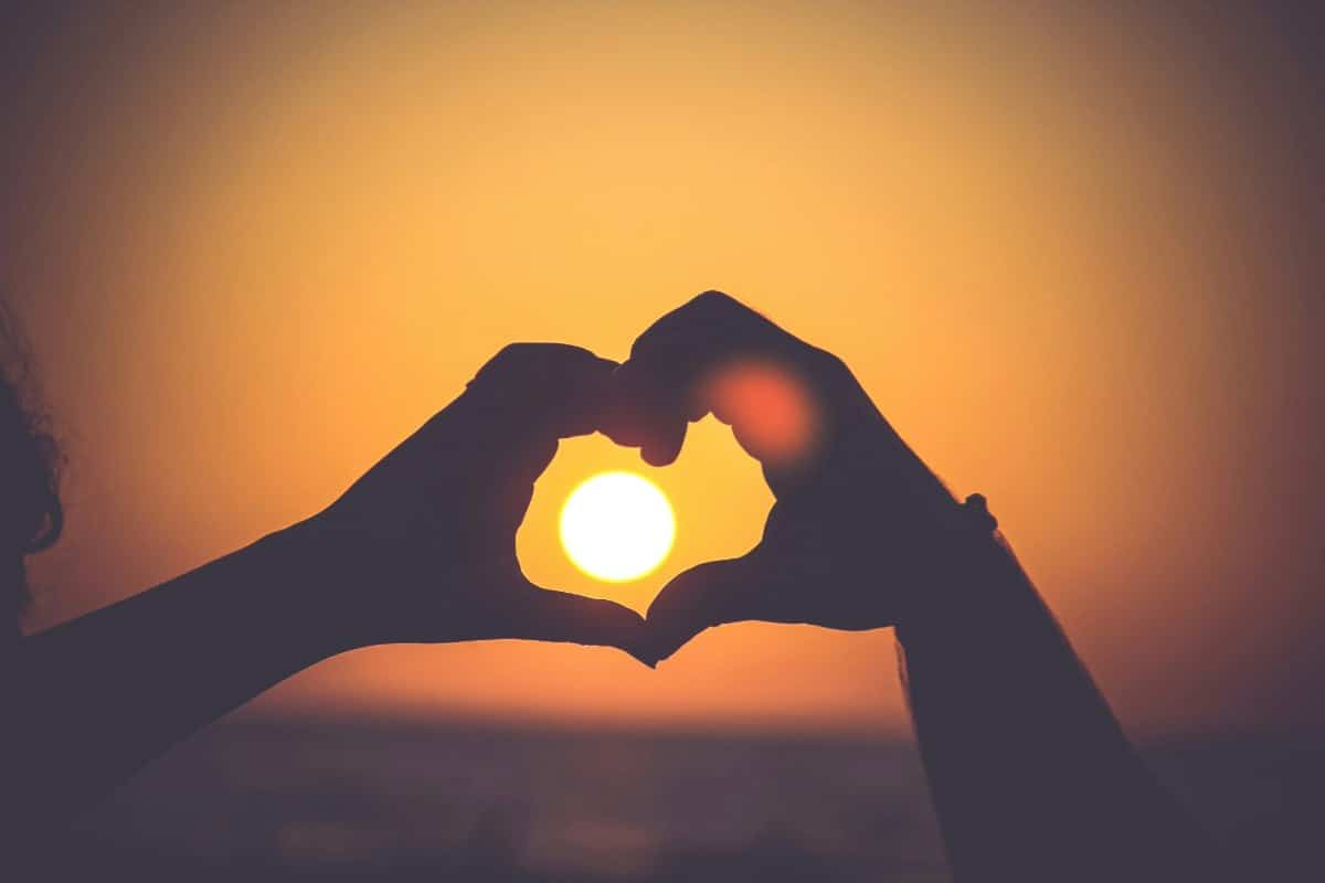 Hands forming a heart shape around the sun at sunset, symbolizing love, unity, and emotional connection in couples therapy.