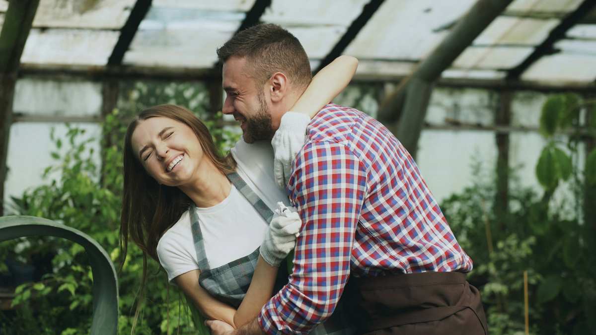 Smiling couple embracing and laughing in a greenhouse, representing joy, trust, and improved communication through couples therapy.