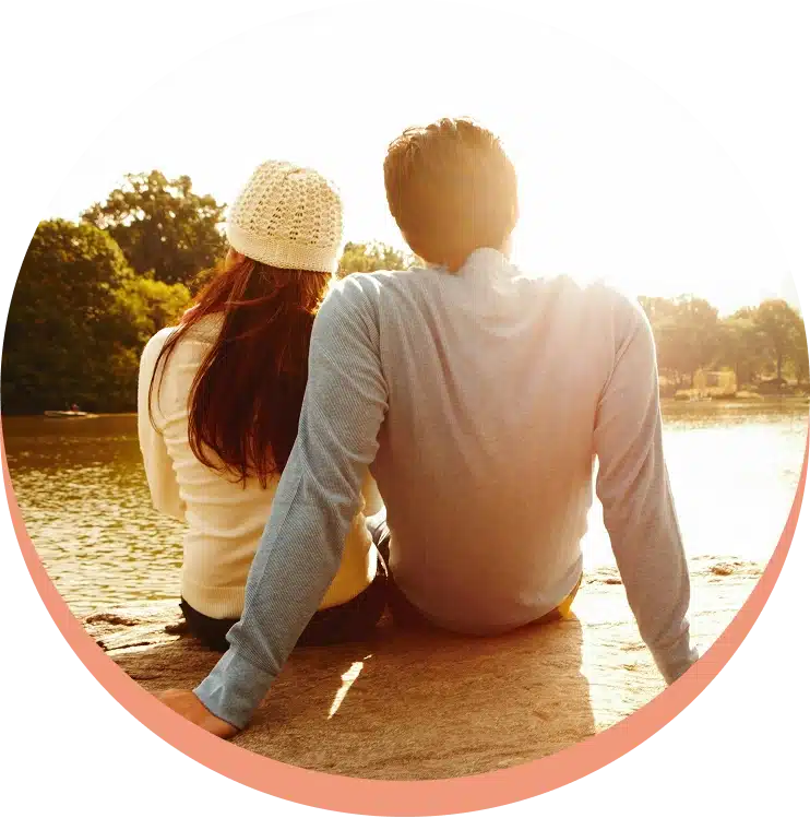 Couple sitting by water, backlit by the sun.