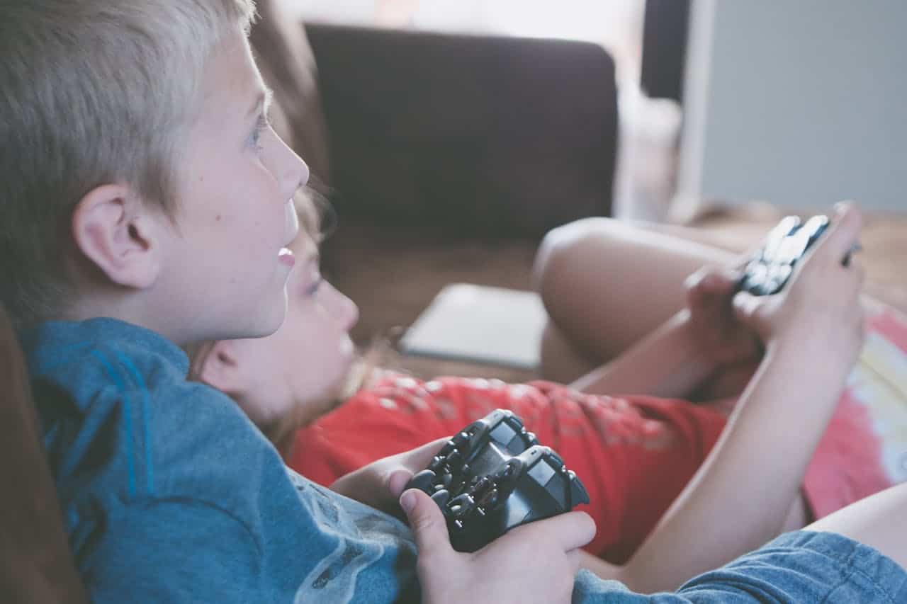 Two children focused on playing video games with controllers, illustrating early signs of technology addiction and anxiety.